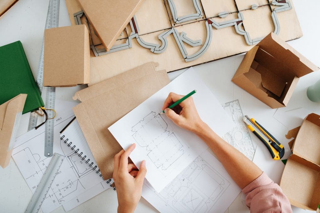 Designer sketching product packaging concepts on a desk with cardboard samples